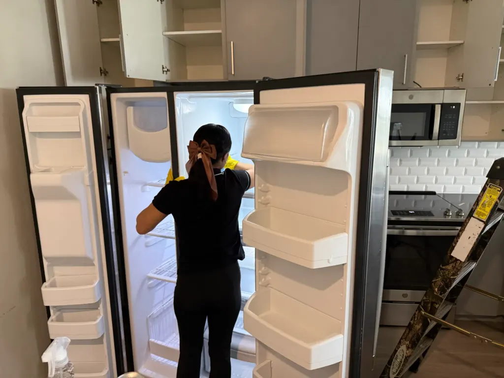 A Reina's Cleaning cleaner wiping out the shelves inside a refrigerator