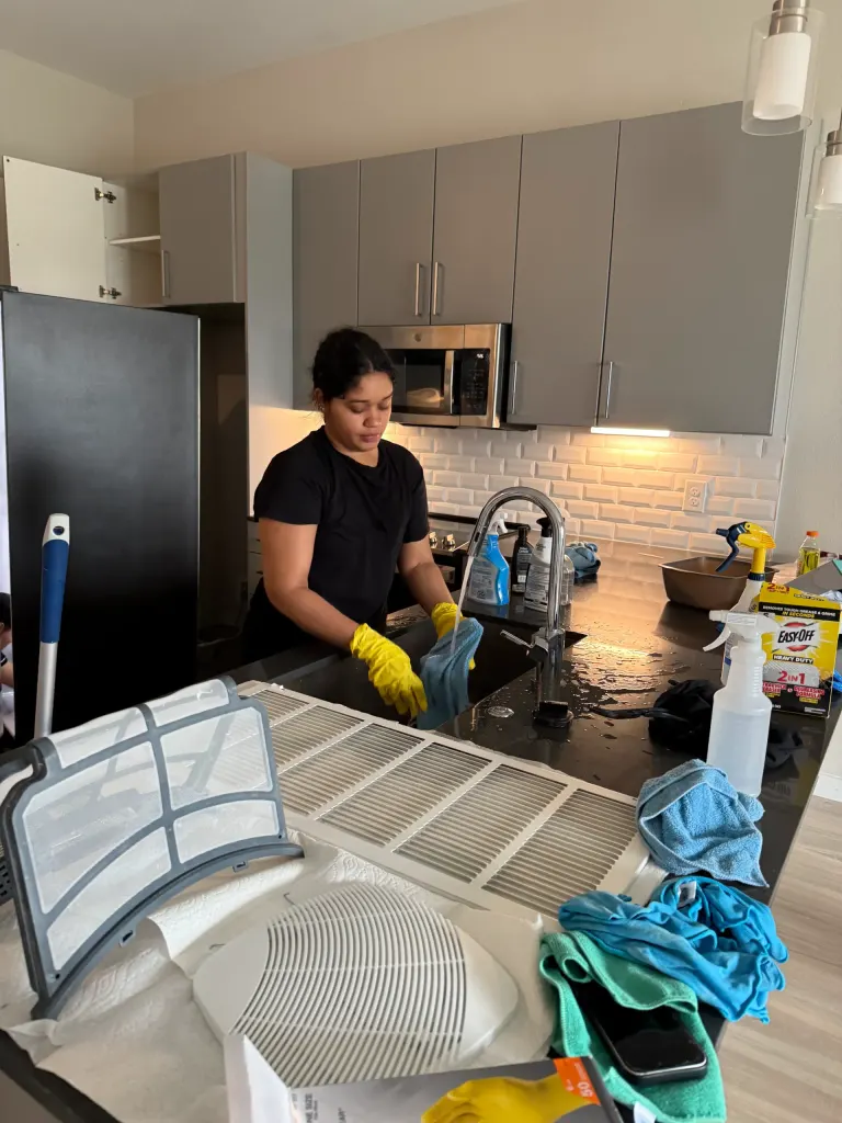 A Reina's Cleaning cleaner washing a vent cover in the kitchen sink