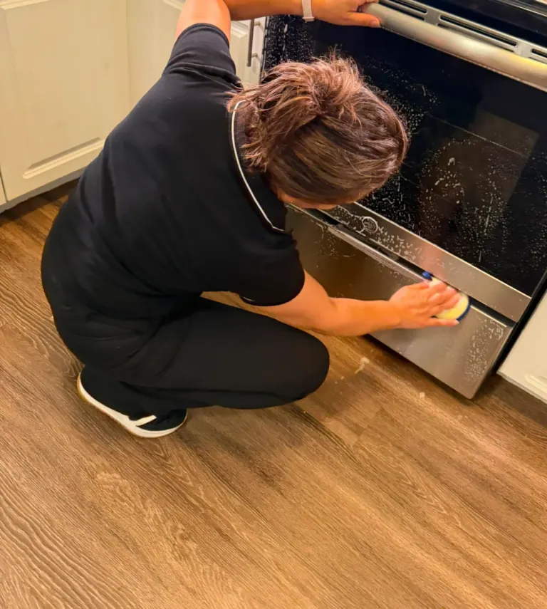 A Reina's Cleaning cleaner wiping an oven door