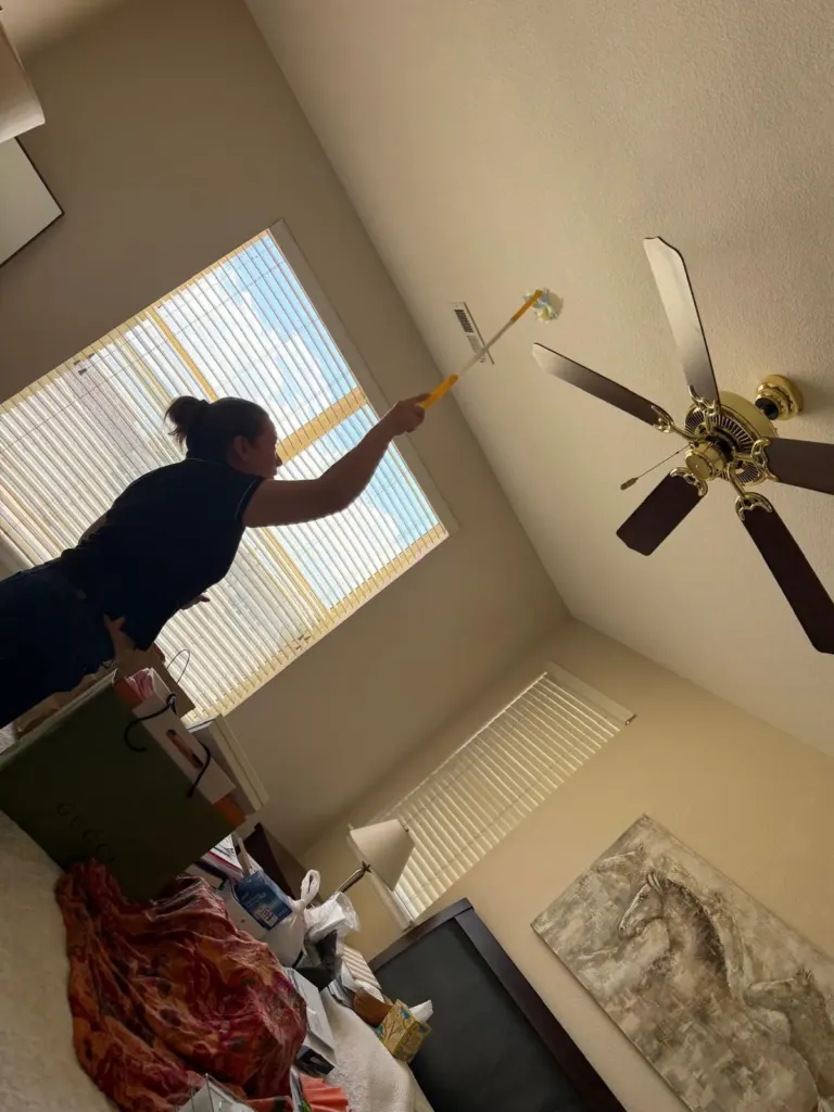 A Reina's Cleaning cleaner dusting a ceiling fan with an extension duster