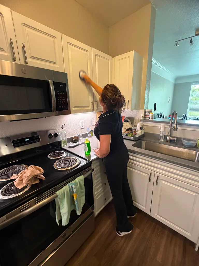 A Reina's Cleaning cleaner wiping kitchen cabinet fronts