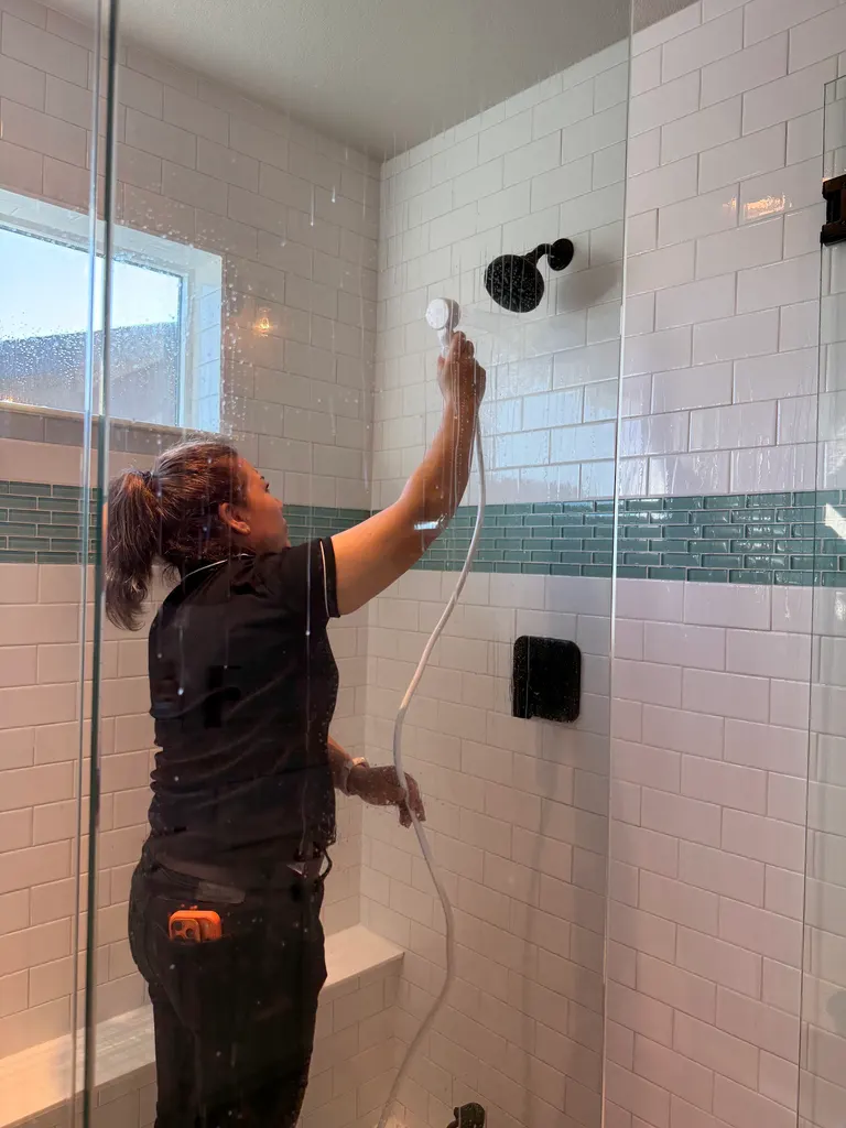 A Reina's Cleaning cleaner washing down a tiled walk-in shower